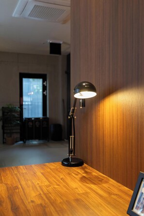 Un bureau en bois, avec une lampe de bureau noire, un tableau encadré et une plante en pot à l’arrière-plan.
