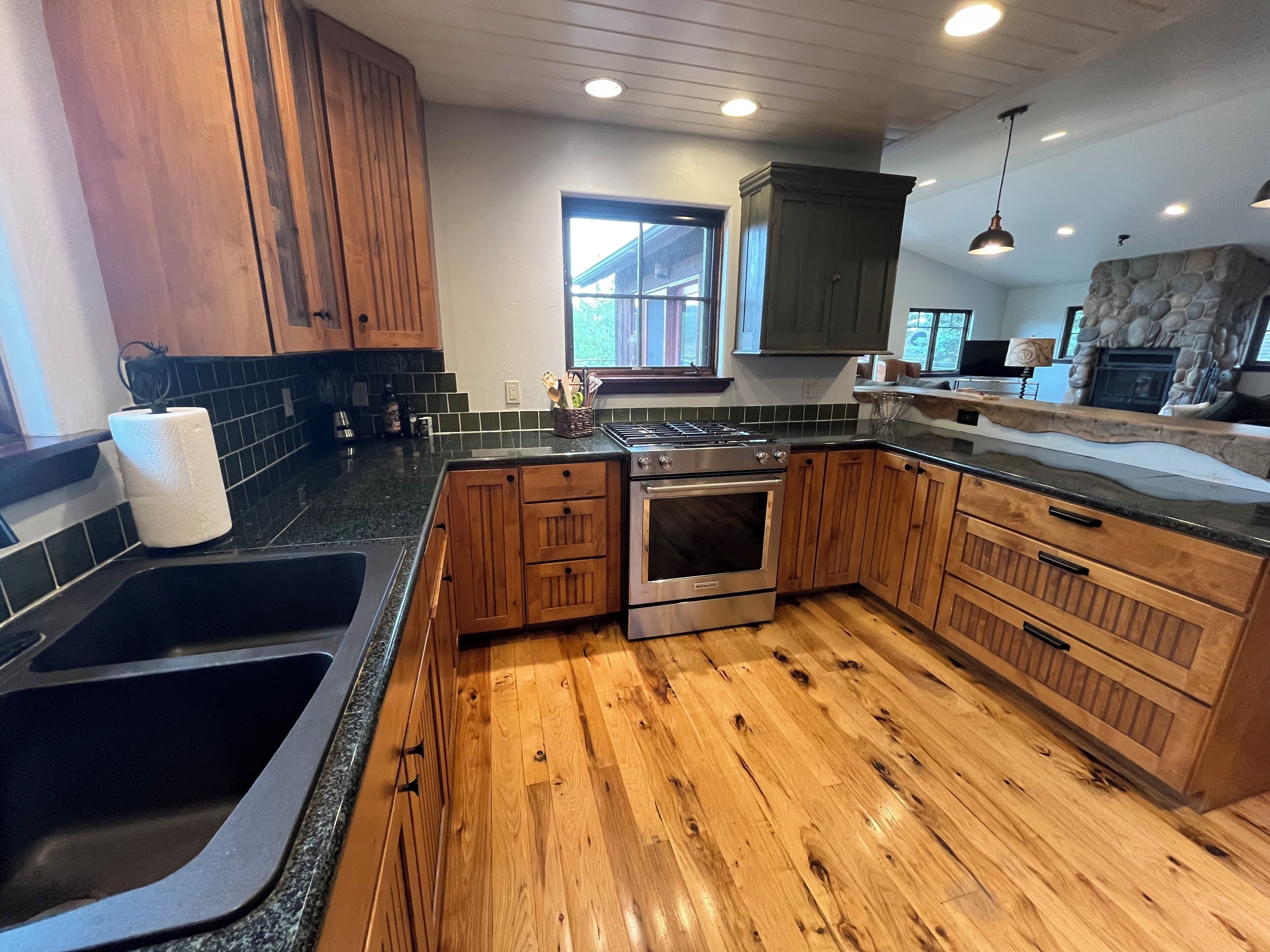 A kitchen with wooden cabinets, a stainless steel stove, a sink, and a stone fireplace.