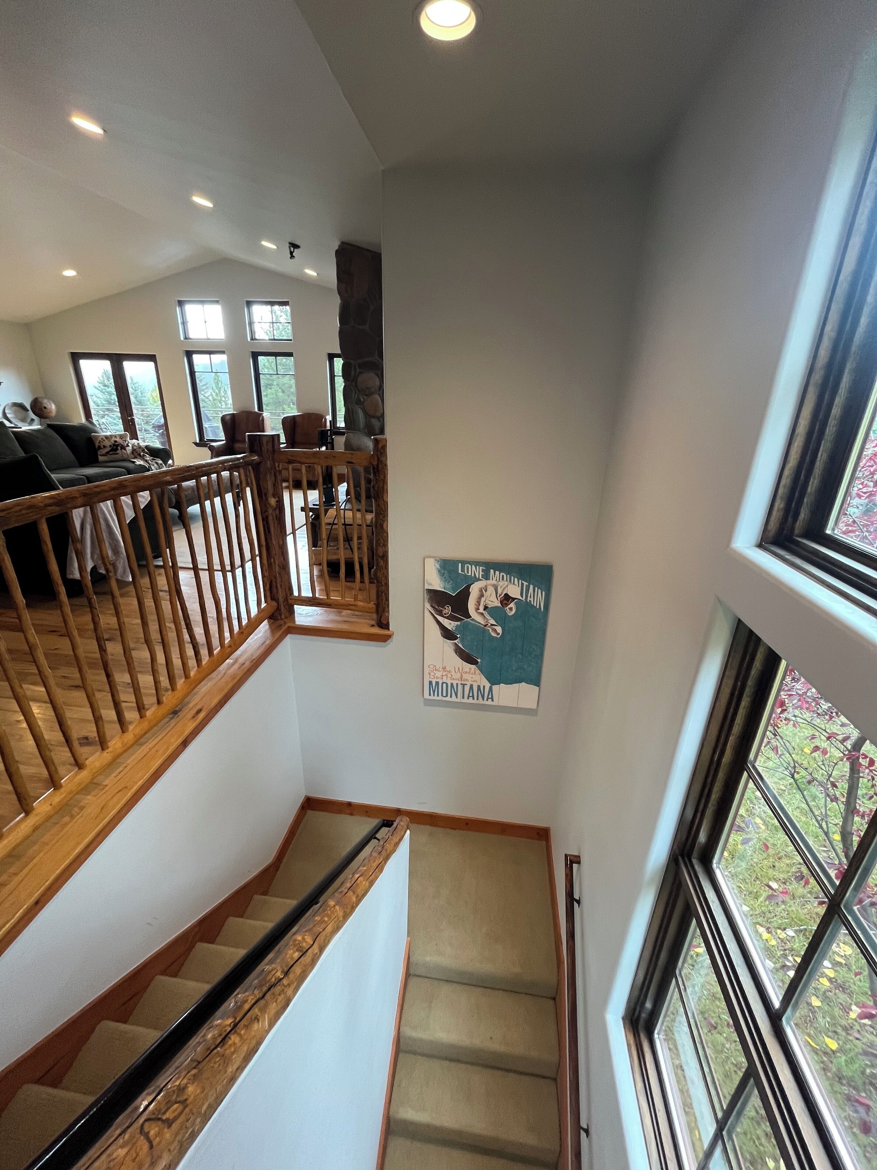 A staircase with wooden railings leading to a living area with a stone fireplace, a dining area with chairs, and a poster of Montana on the wall.