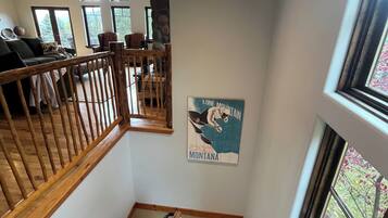 A staircase with wooden railings leading to a living area with a stone fireplace, a dining area with chairs, and a poster of Montana on the wall.