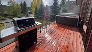 Una terrazza in legno con una griglia Weber e una vasca idromassaggio.