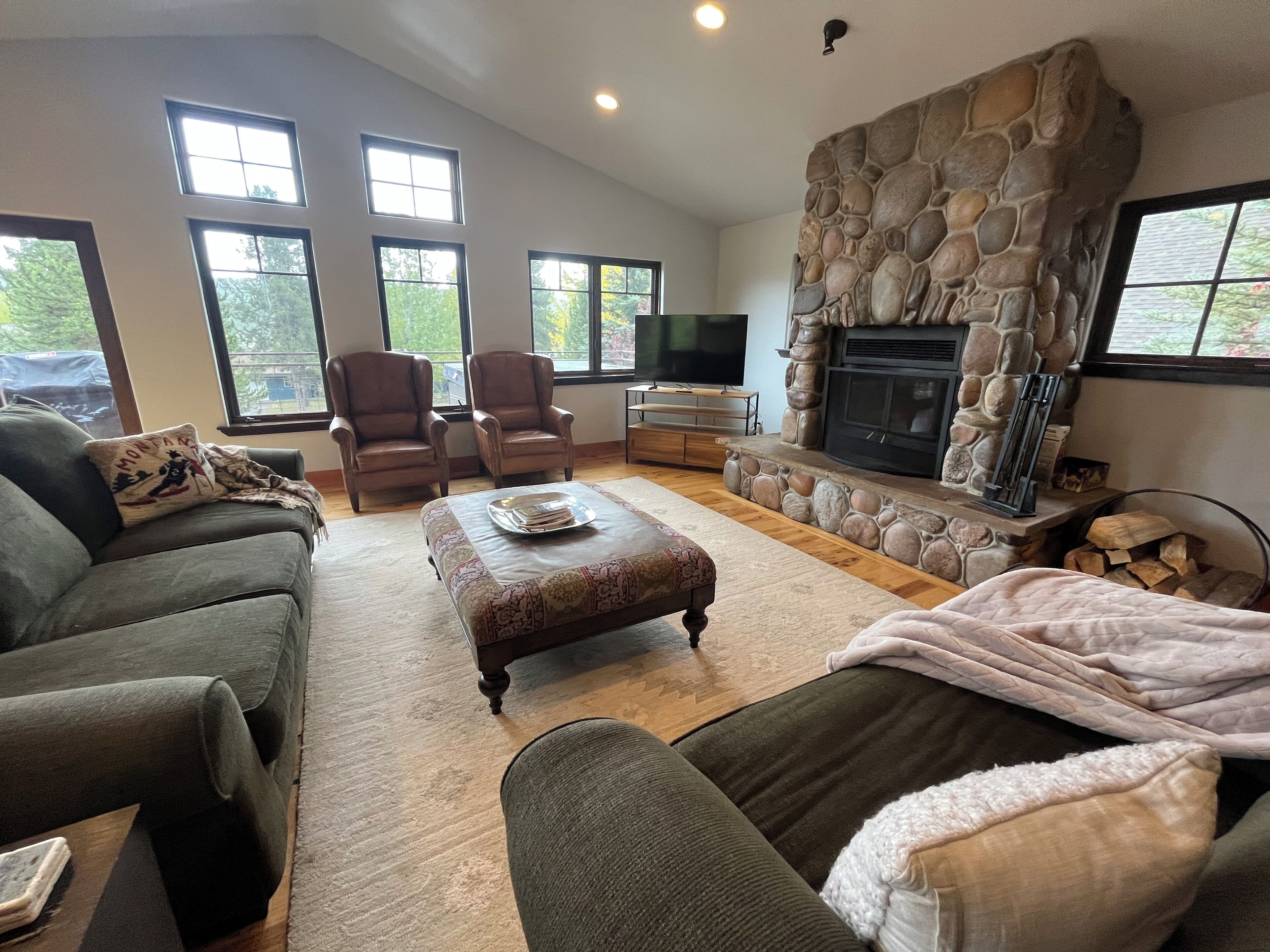 A spacious living room with a stone fireplace, comfortable seating, and large windows.