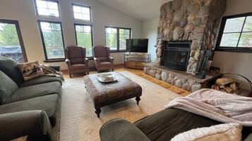 A spacious living room with a stone fireplace, comfortable seating, and large windows.