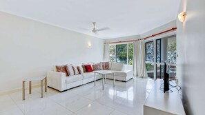 A modern living room with a white sofa, a coffee table, and a TV. - Ulysses 2 Beach front Apartment (Wongaling Beach)