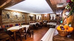 Un coin repas rustique avec des tables et des bancs en bois, des murs en pierre et un panier de fruits posé sur une table en bois.