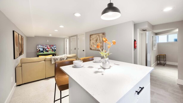 Una sala de estar moderna con un sofá color beige, una mesa de centro y un televisor mostrando un partido deportivo.