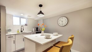 Una cocina moderna con armarios blancos, una isla blanca, una silla amarilla, un reloj y un jarrón con flores.