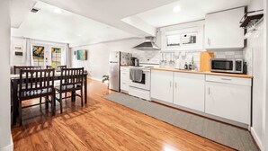 A modern kitchen with white cabinets, a wooden dining table, and a large window. - Spacious 2BR Home, Backyard Parking & UW (Seattle)