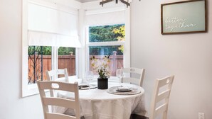 A dining area with a table set for two, white chairs, a chandelier, and a framed sign on the wall. - Modern 2BR Home in Ravenna, Near UW, Green Lake (Seattle)