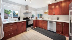 A modern kitchen with wooden cabinets, a stainless steel range hood, and a large window providing natural light. - Modern 2BR Home in Ravenna, Near UW, Green Lake (Seattle)