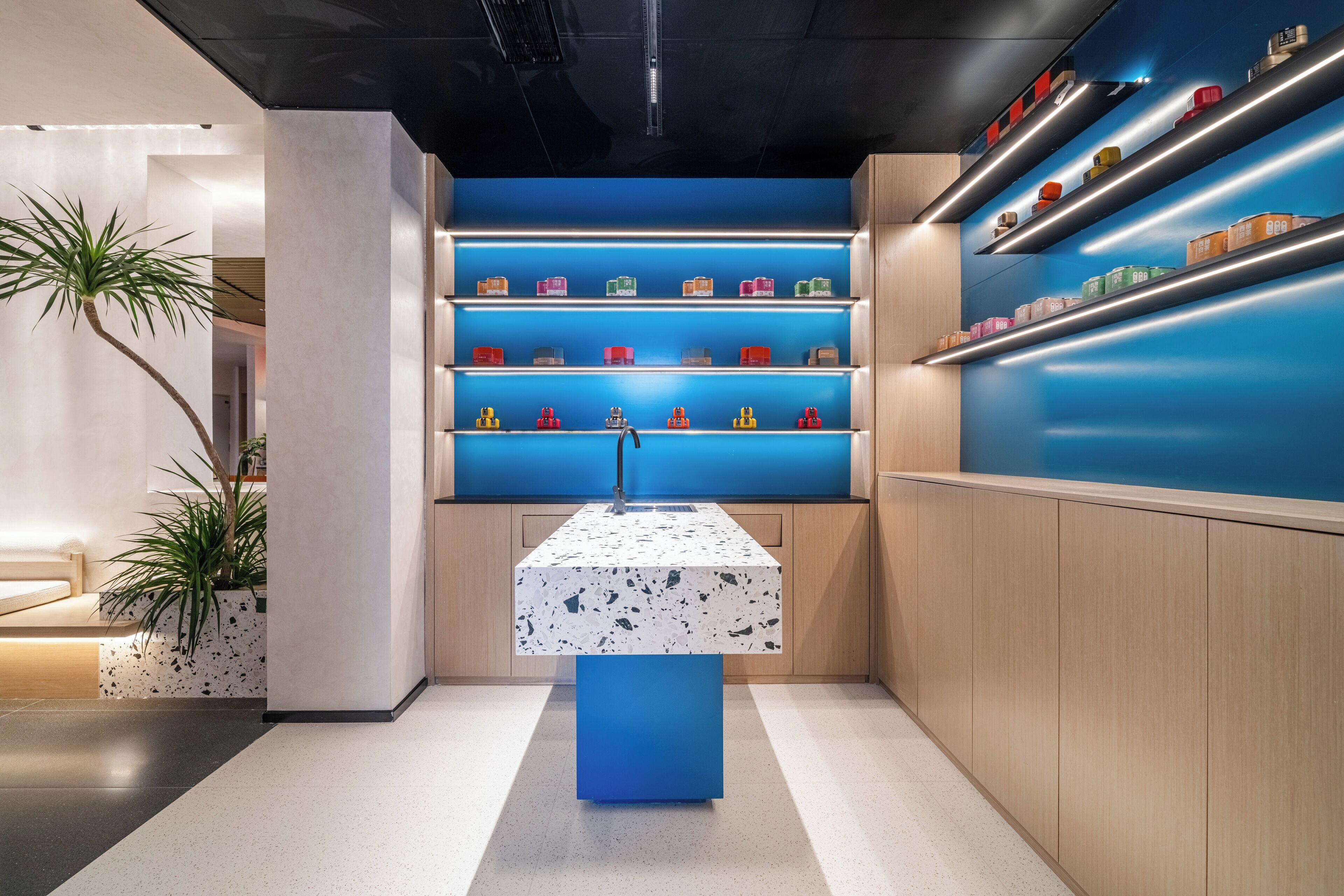 Un interior moderno con una isla central, estantes con objetos de colores y una planta en maceta.