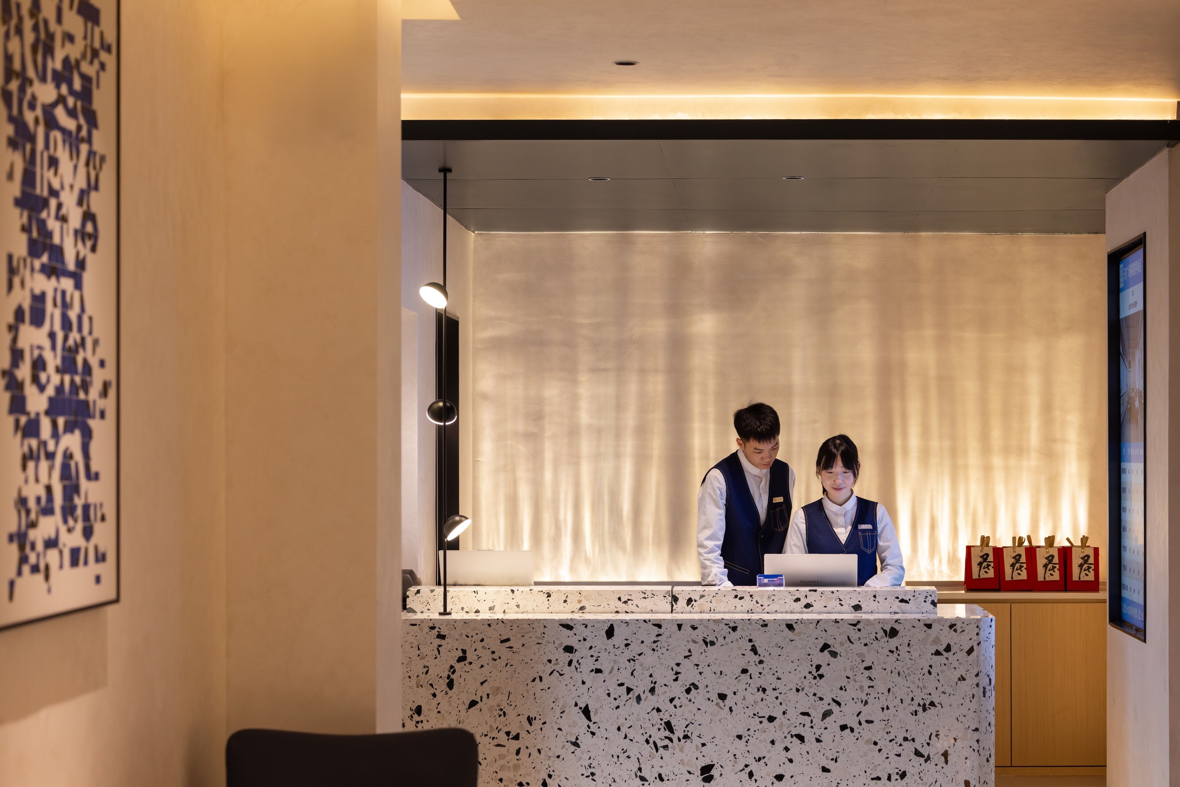 A reception desk with two staff members, a modern interior design, and a window with curtains.