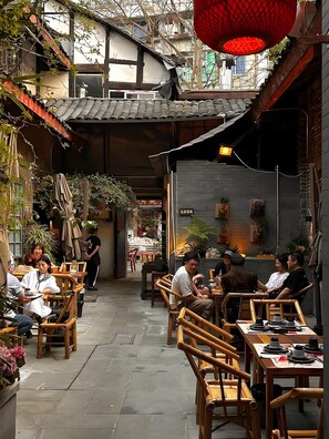Un espace de restauration en plein air, avec des chaises et des tables en bambou, entouré de plantes et d’une architecture traditionnelle.