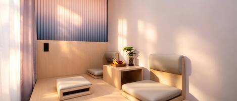 A modern room with a wooden desk, two cushioned chairs, a small side table with a plant, and a window with vertical blinds.