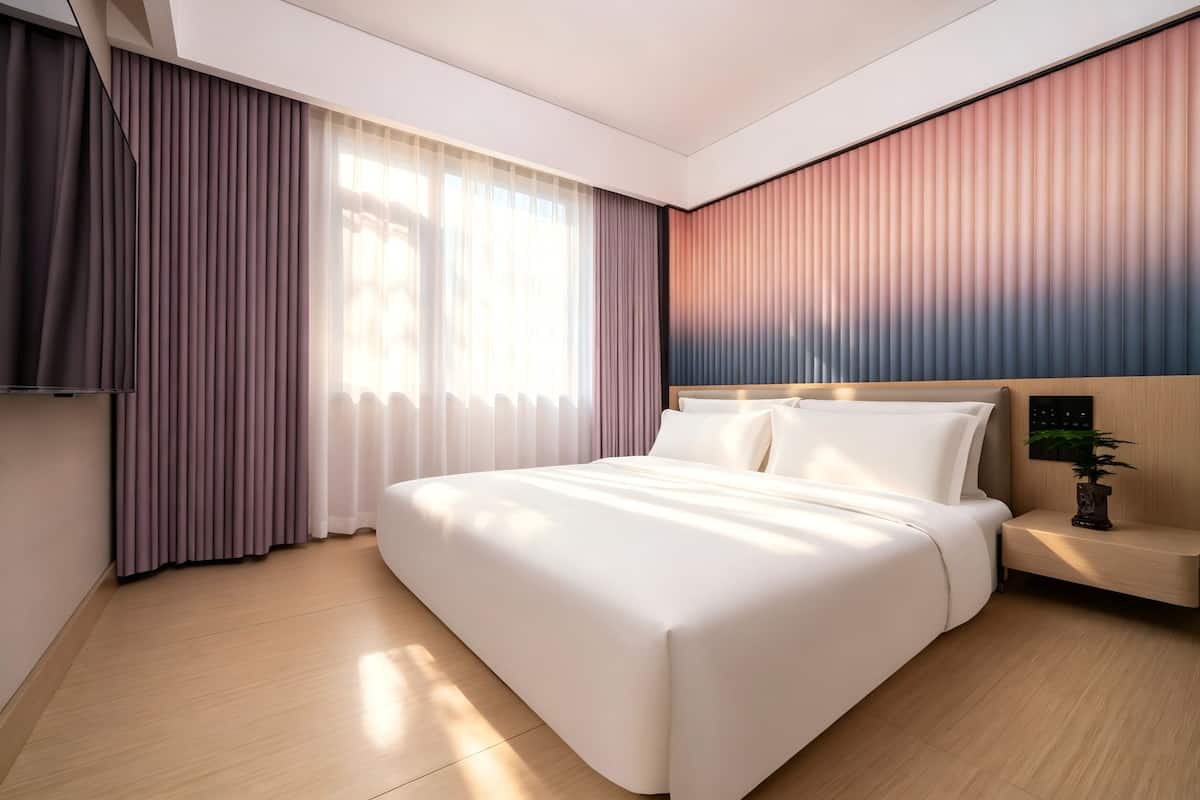A modern hotel room with a large bed, a bedside table, a TV, and a window with curtains.