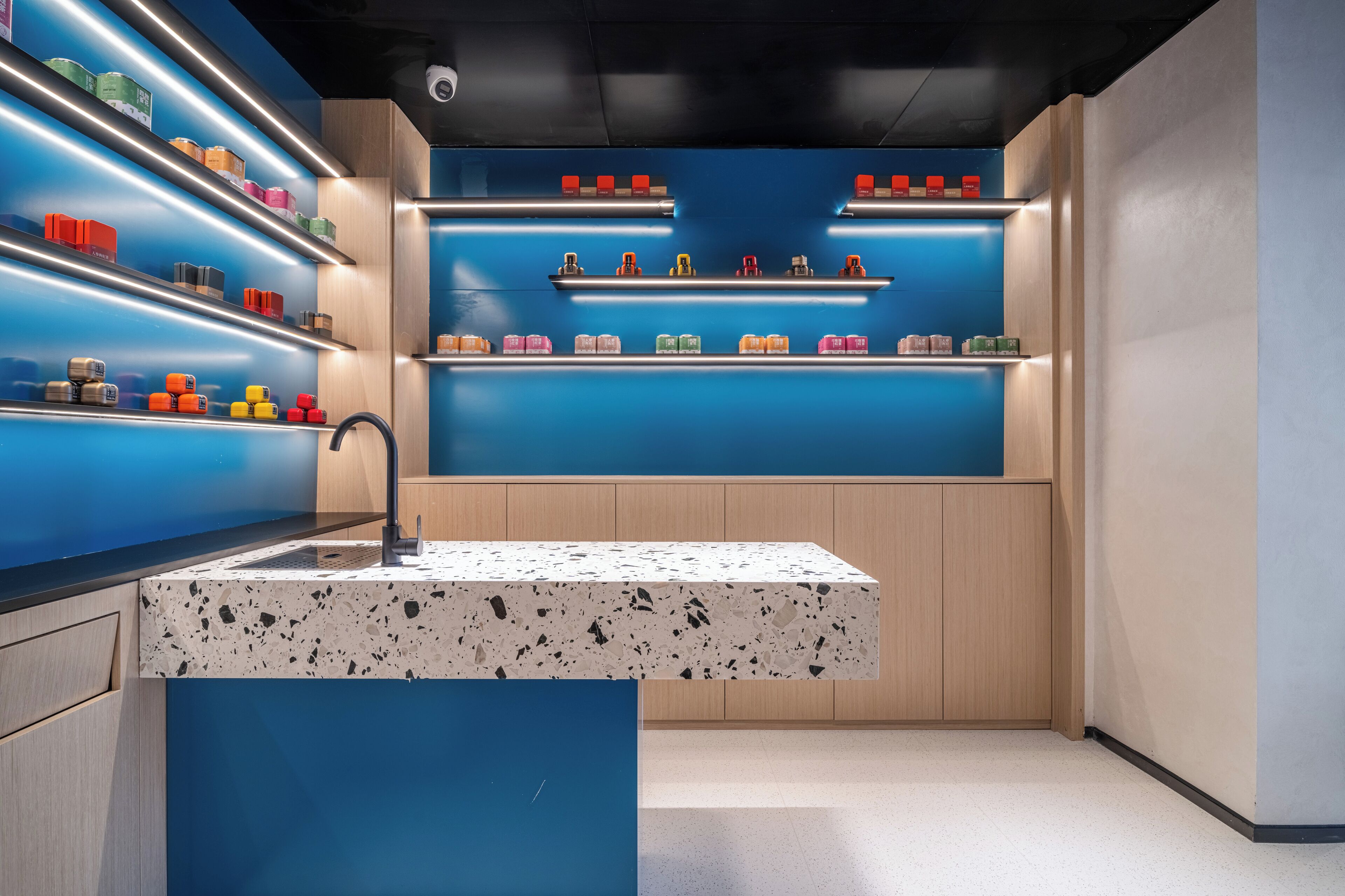 A modern kitchen with a granite countertop, blue cabinetry, and a variety of colorful containers on shelves.
