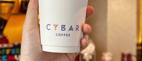 A hand holding a CYBAR COFFEE cup with a white lid.