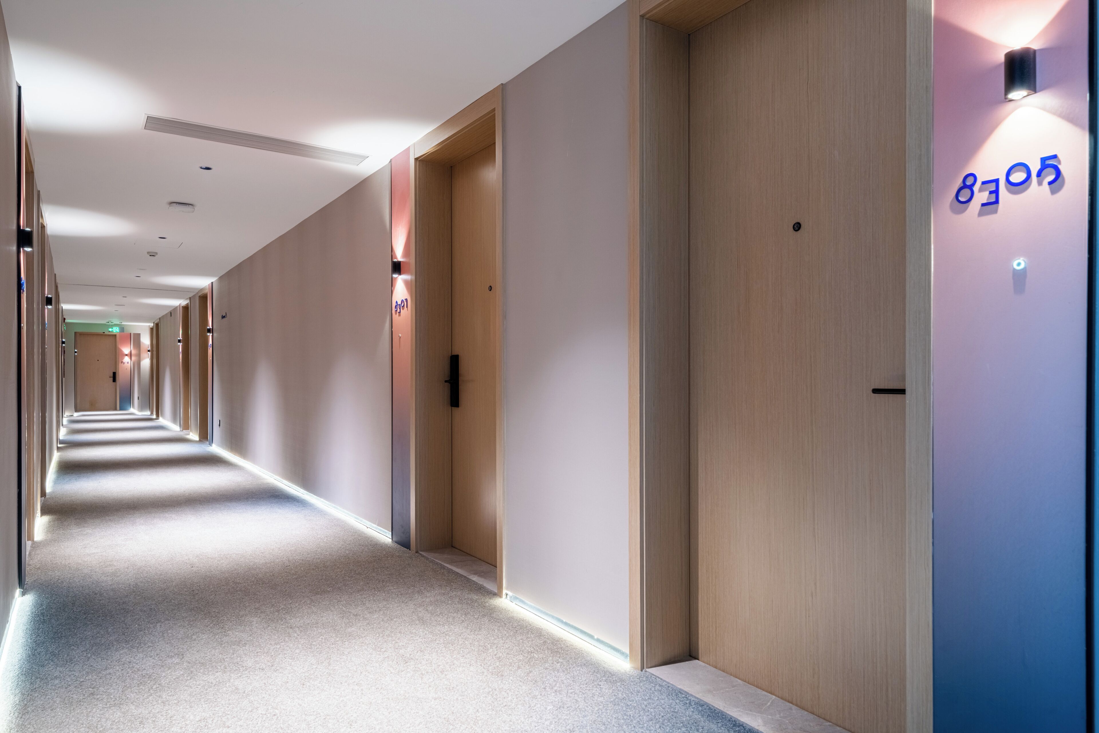 A hotel corridor with multiple doors, a carpeted floor, and a light fixture on the wall.