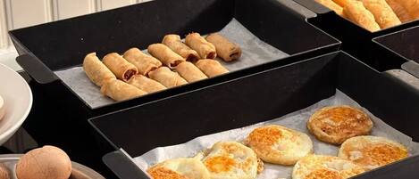 Un bufé con diversos alimentos, incluyendo rollitos primavera y pasteles, dispuestos en bandejas negras.
