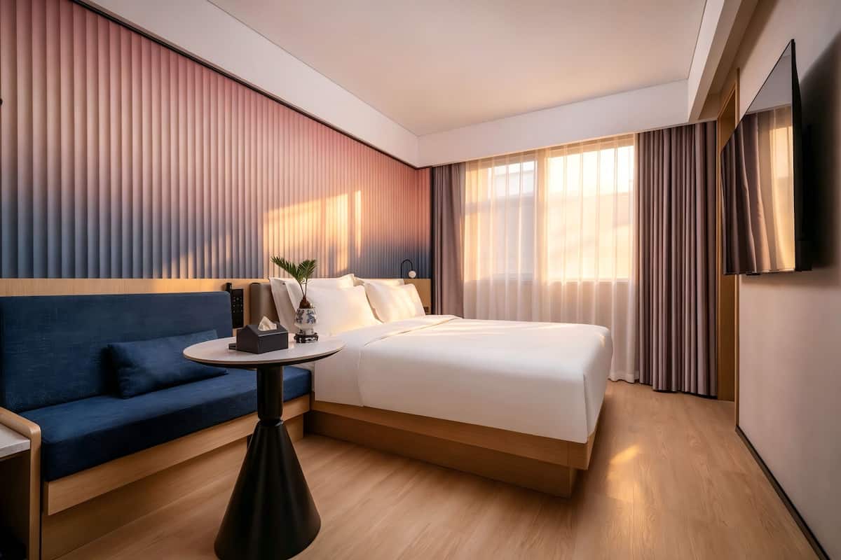 A hotel room with a bed, a sofa, a small table, a TV, and a window with curtains.