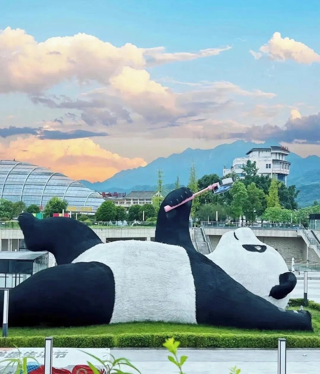 A large panda sculpture lying on the ground with a cityscape in the background.