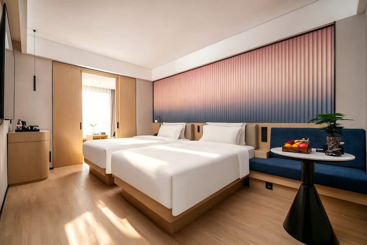 A modern hotel room with two beds, a sofa, a small table, and a TV.