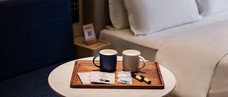 Quarto de hotel com cama, mesa de cabeceira com um tabuleiro contendo duas chávenas, caneta e algumas cartas.