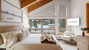 A bedroom with a large bed, a chair, a dresser, a TV, and a window with a view of a snowy landscape. - 11 Bedroom Duplex - Vail Village (Vail)