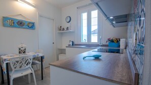 A modern kitchen with a wooden countertop, a dining area with a white table and chairs, a clock on the wall, and a window providing natural light. - Cosmopoli La Vela - Studio in Portoferraio (Portoferraio)