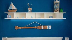 A room with a blue wall, a white bed, and a wooden wall hanging. - Cosmopoli La Vela - Studio in Portoferraio (Portoferraio)