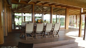 A covered outdoor dining area with wooden tables and chairs, large windows, and a view of greenery. - Beautiful villa near Lake Trasimeno (Castiglione del Lago)