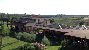 A large house with a covered patio area, surrounded by lush greenery and a vineyard in the background. - Beautiful villa near Lake Trasimeno (Castiglione del Lago)