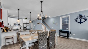 Une cuisine moderne avec des meubles blancs, des appareils en acier inoxydable et un coin repas agrémenté de chaises à motifs et d’une table en bois.