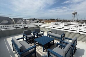 Une terrasse sur le toit, aménagée avec du mobilier d’extérieur, d’où l’on peut admirer un château d’eau et une rangée de maisons en arrière-plan.