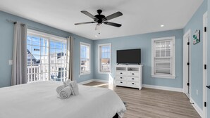 Une chambre avec un grand lit, un ventilateur de plafond, une télévision et une vue sur l’extérieur.