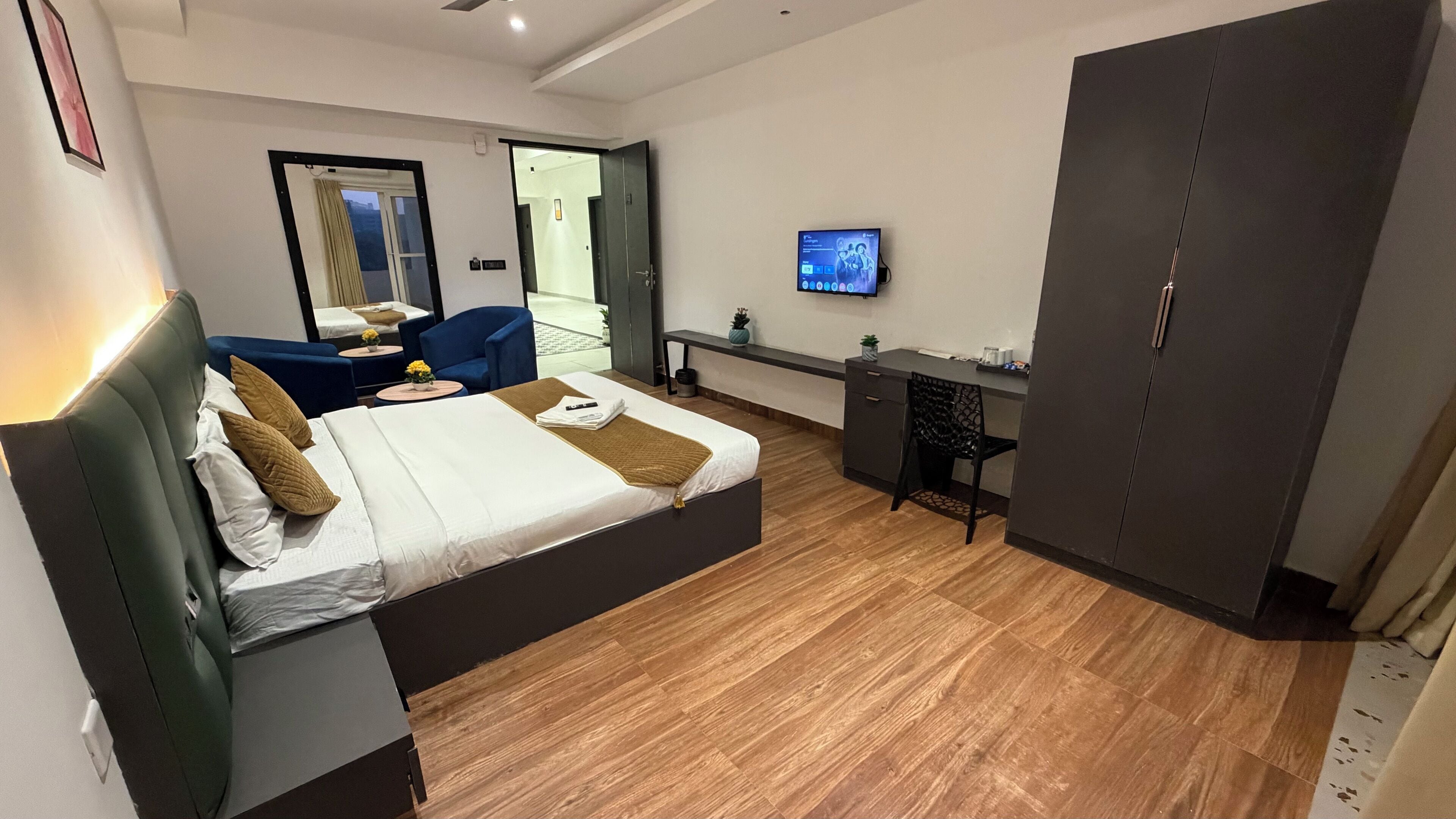 A modern hotel room with a bed, a desk, a chair, a wardrobe, and a TV.