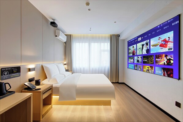 A modern hotel room with a large bed, a desk with a phone and a coffee maker, a wall-mounted TV displaying various shows, and a window with curtains. - Zhesu Select Hotel (Taiyuan)