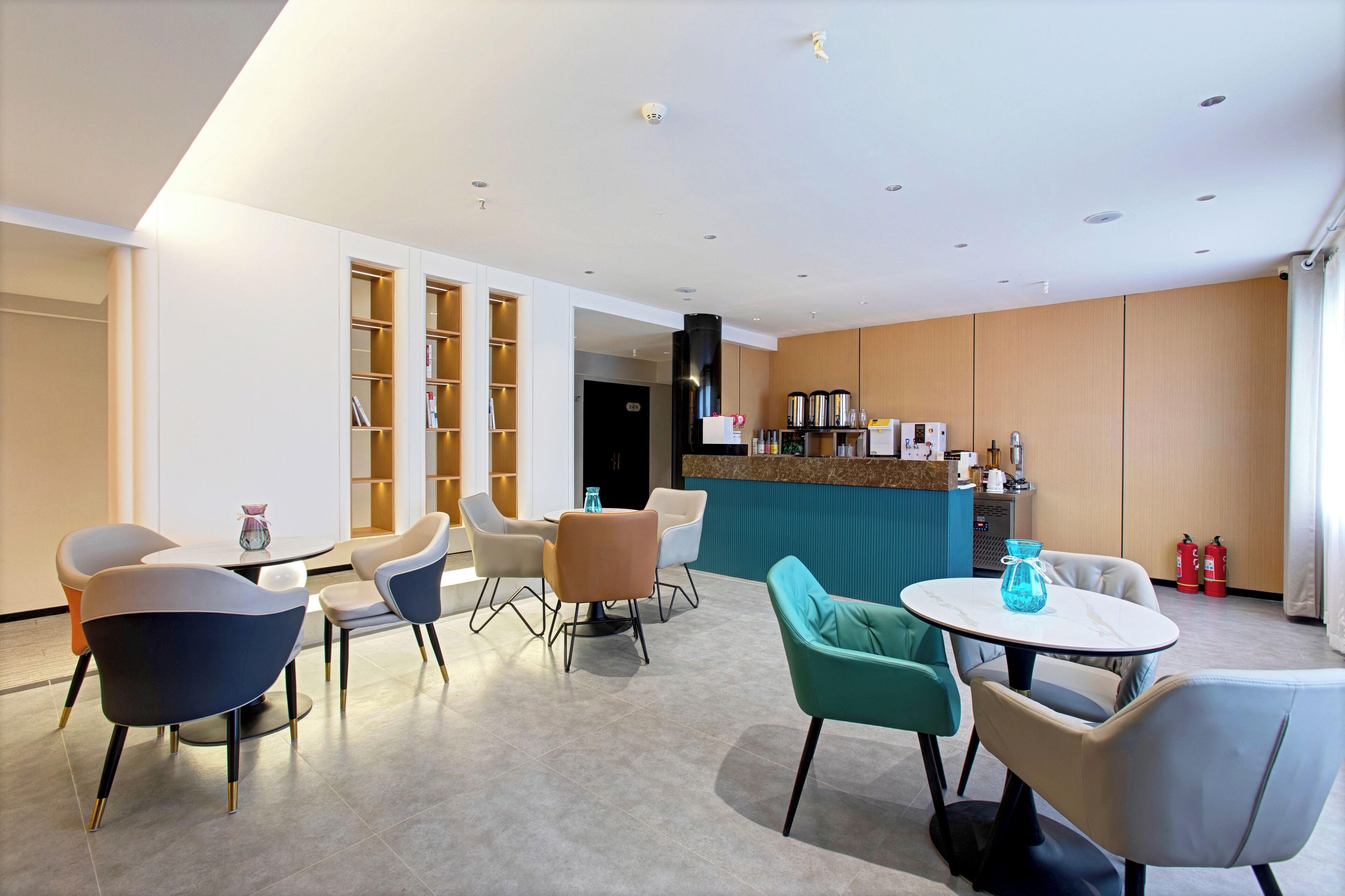 A modern hotel lobby with a reception desk, seating area, and a kitchen in the background.