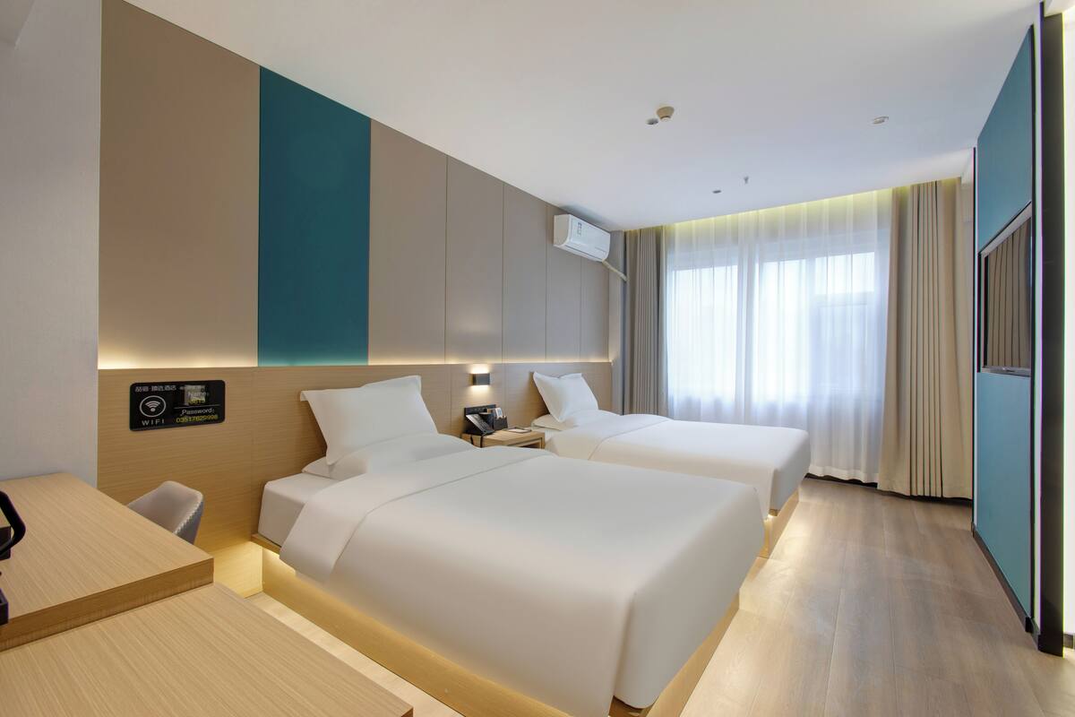 A hotel room with two beds, a desk, a chair, a nightstand, an air conditioning unit, and a TV.
