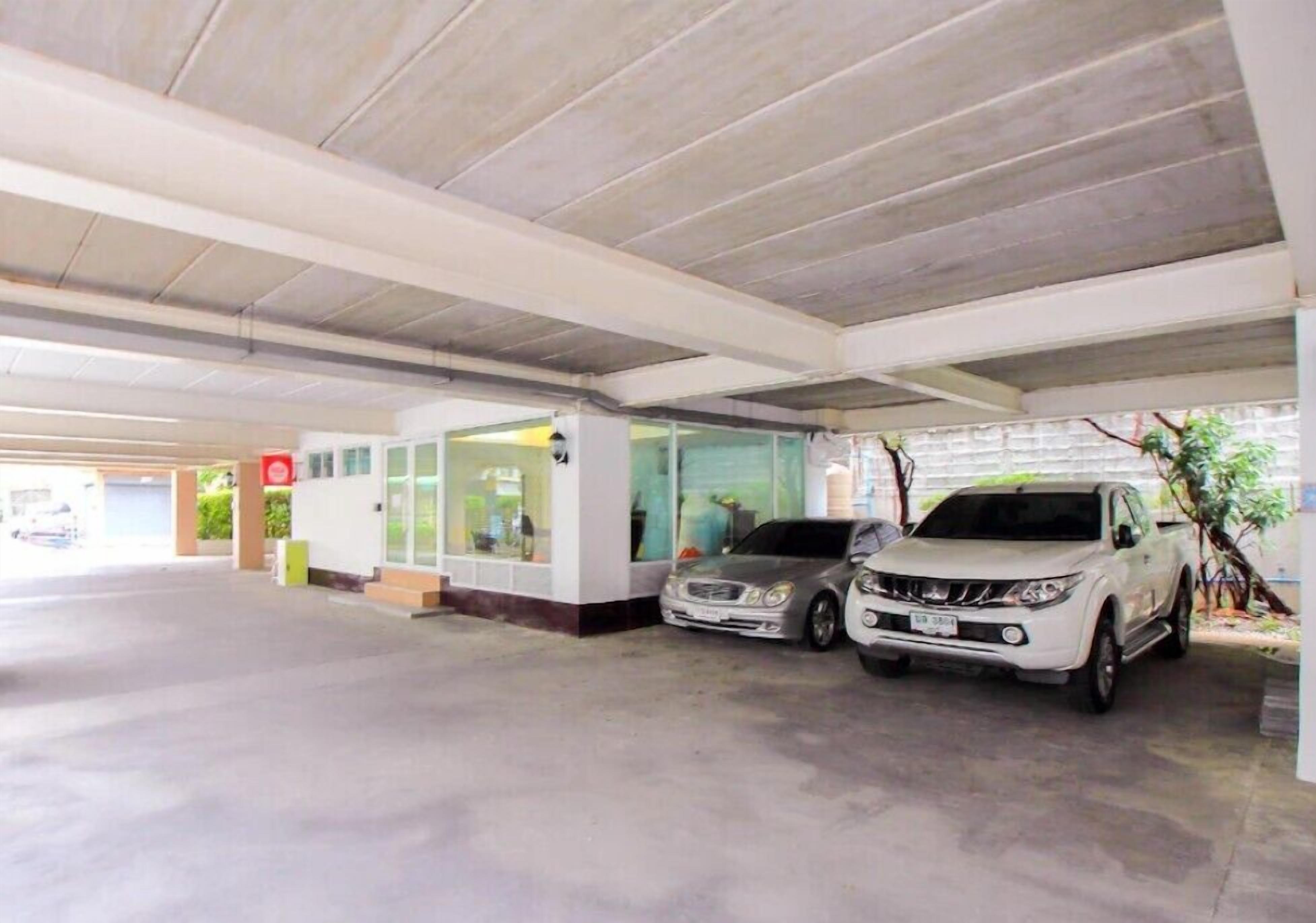 A covered parking area with two cars parked, a building with glass doors, and a visible sign.