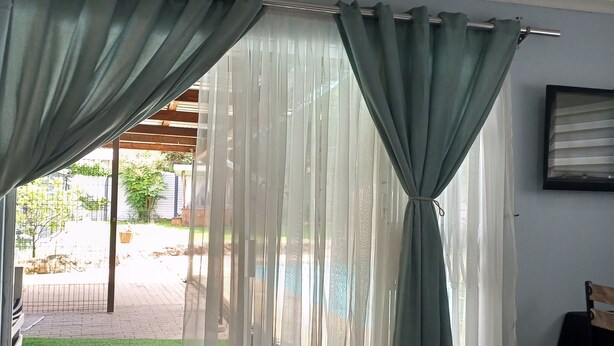 Et værelse med en skydedør, der fører ud til en terrasse med velplejet græsplæne og en træpergola.