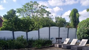 Et rektangulært swimmingpool med klart, blåt vand, omgivet af en betonflisebelagt terrasse. Liggestole og et lille bord ses i baggrunden.
