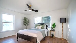 A bedroom with a bed, a ceiling fan, a floor lamp, and a window.