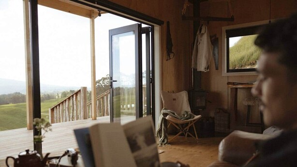 A cozy room with a large window, a chair, a table with a teapot, and a fireplace. - Sunsets, outdoor bath, mountain views, fire pit (Marotiri)