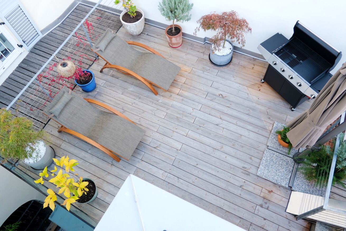 A rooftop patio with a grill, potted plants, and outdoor furniture.
