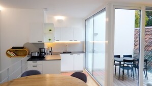 A modern kitchen with white cabinets, a wooden dining table, and a glass sliding door leading to an outdoor seating area. - Apartment Lauben- Alpstay (Merano)