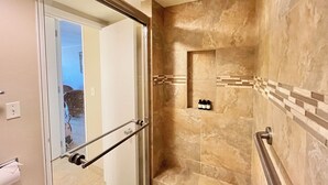 A modern bathroom with a glass door, a shower with a built-in shelf, and a tiled wall. - Guest Favorite: Beachfront Studio Turtles, Monk Seals, Surf & Mountain View (Lahaina)