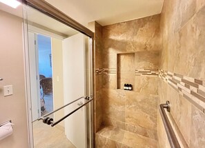 Ein modernes Badezimmer mit Glastür, einer Dusche mit integriertem Ablagebereich und einer gefliesten Wand.