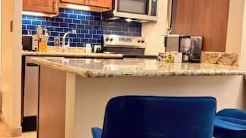 A kitchen with wooden cabinets, a microwave, a stove, and a sink. There are two blue chairs with gold legs.