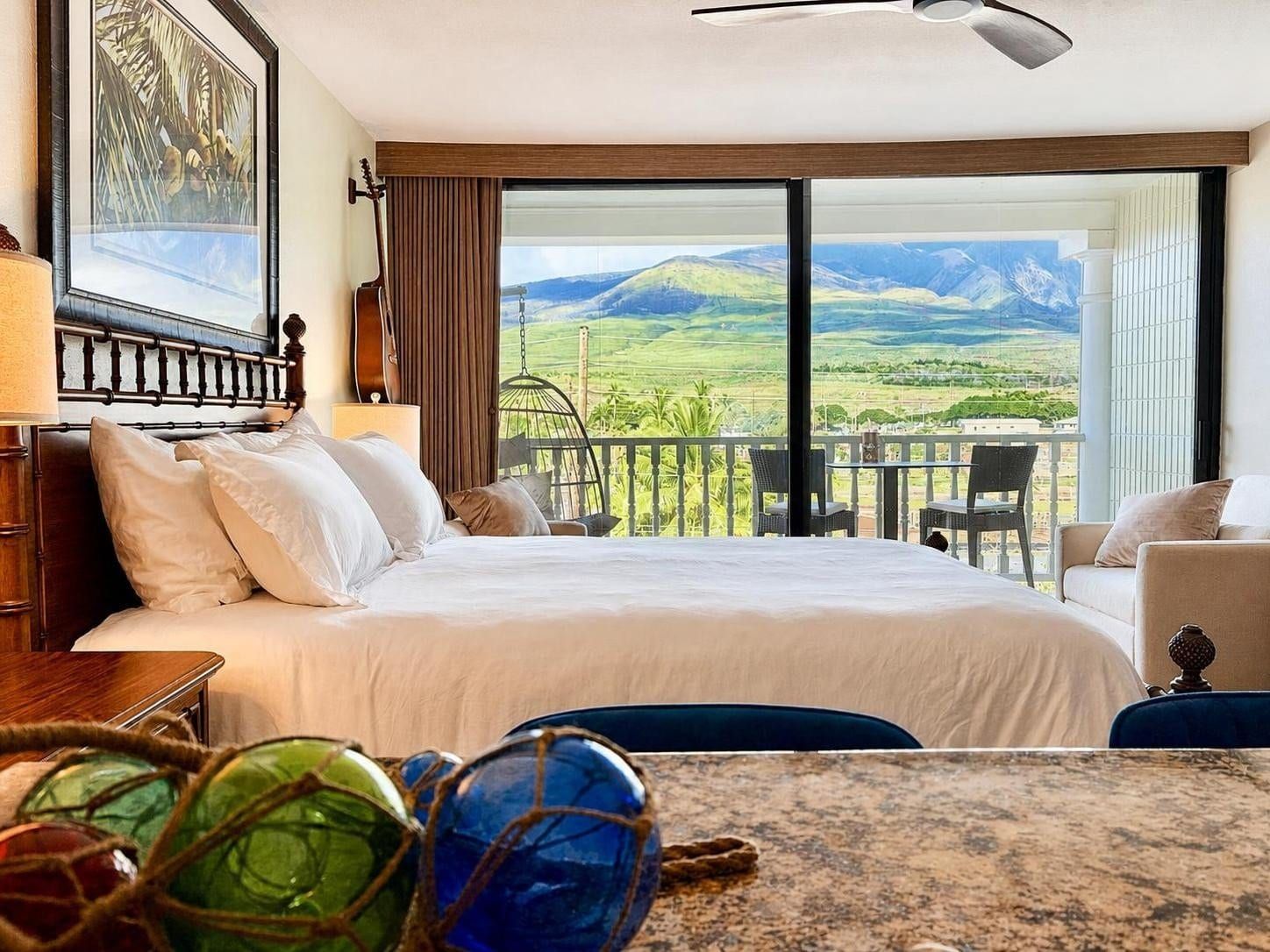 Une chambre d’hôtel avec un lit, une vue sur la campagne, un balcon avec des chaises et une guitare accrochée au mur.